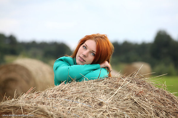 Blue-eyed redhead nude by a haystack