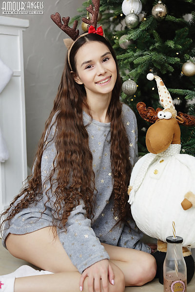 Long-haired brunette teen stripping by the Christmas tree