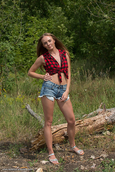 Freckled girl takes off her jean shorts in a field