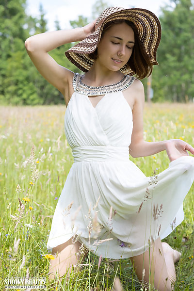 Brunette teen takes off her dress in a field
