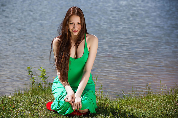 Long-haired brunette  lifts up her dress by a lake