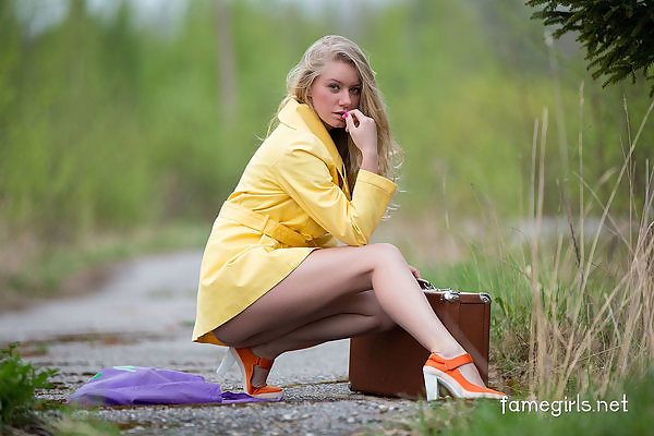 Sexy blonde takes off her yellow coat by a field