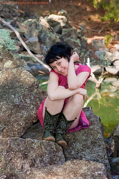 Tattooed girl with black hair stripping on some rocks