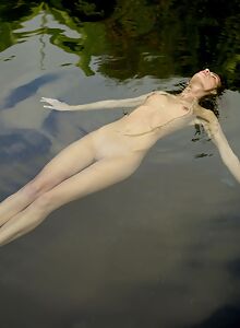 Freckled brunette floating nude in a pool