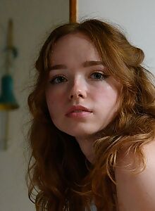 Cute shaved redhead naked by a window