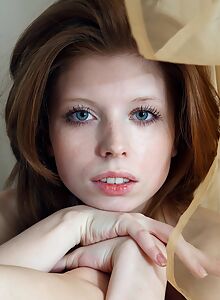 Freckled redhead with fair skin naked by a window