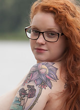 Curvy redhead with tattoos shows off her big tits in a field